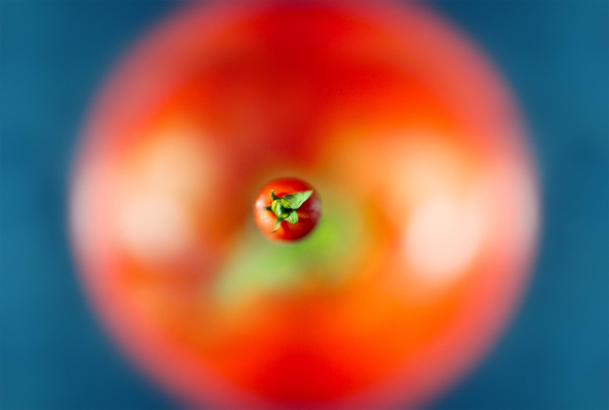 a water droplet shot from above with a tomato below it, reflected into the drop itself