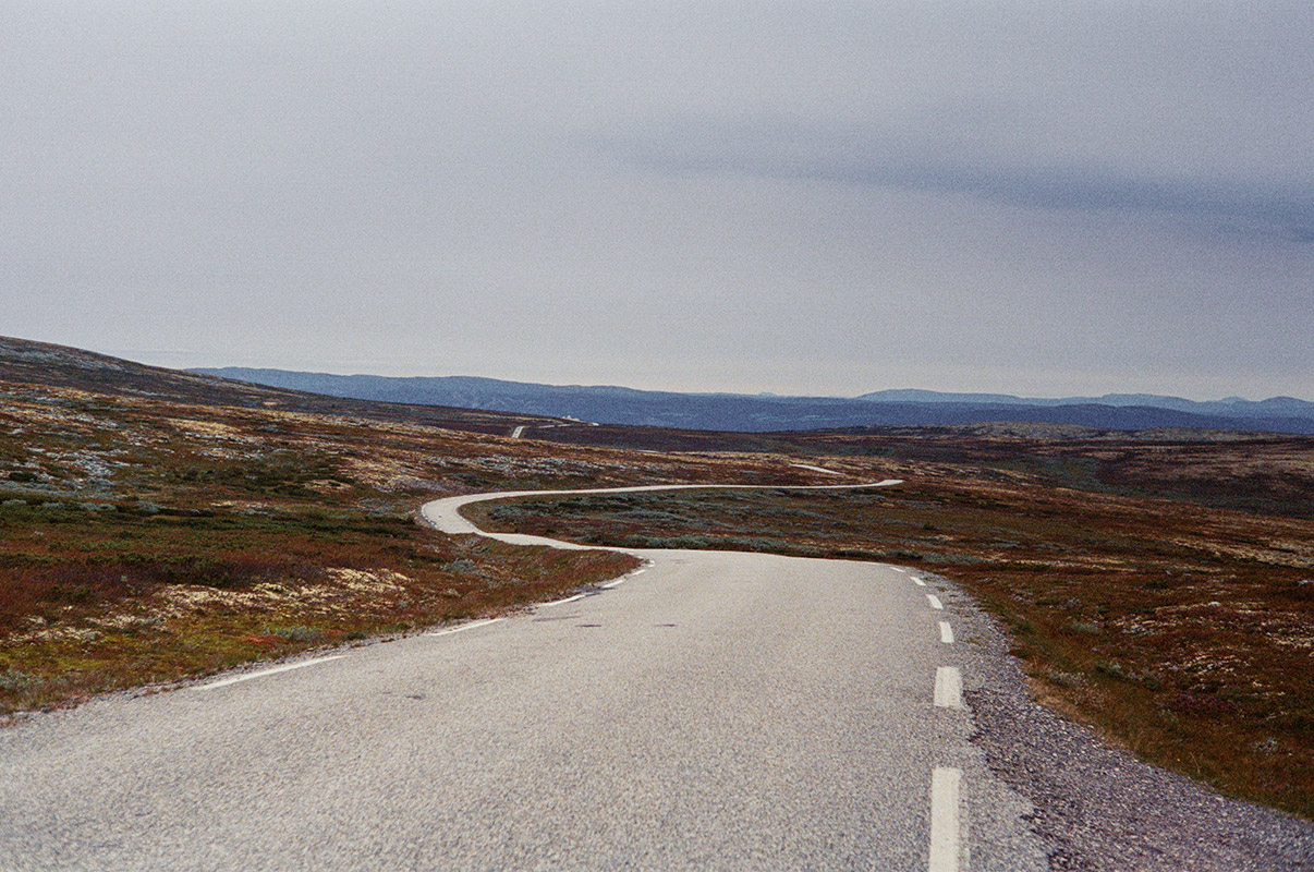 an empty winding road with normal-length dashed outer lines. the road cuts through barren moorland. it's overcast.