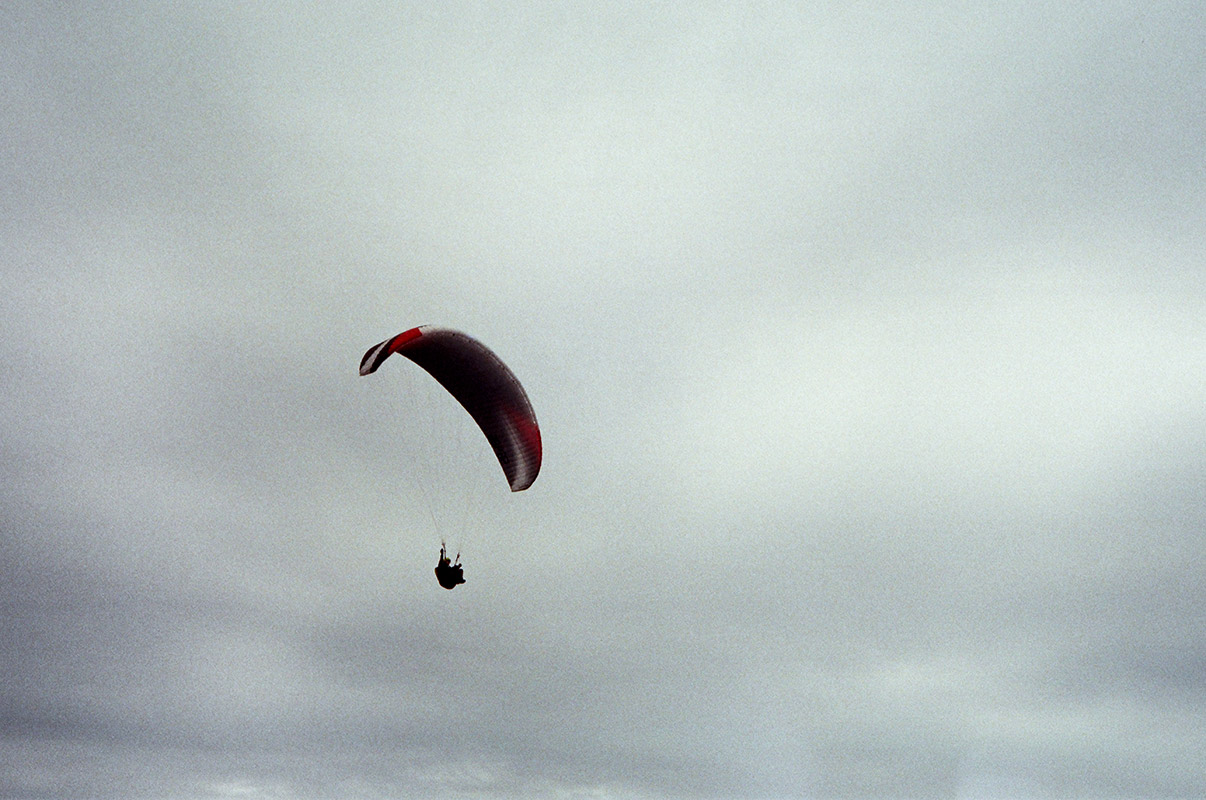 a lone paraglier against a cloudy gray sky.