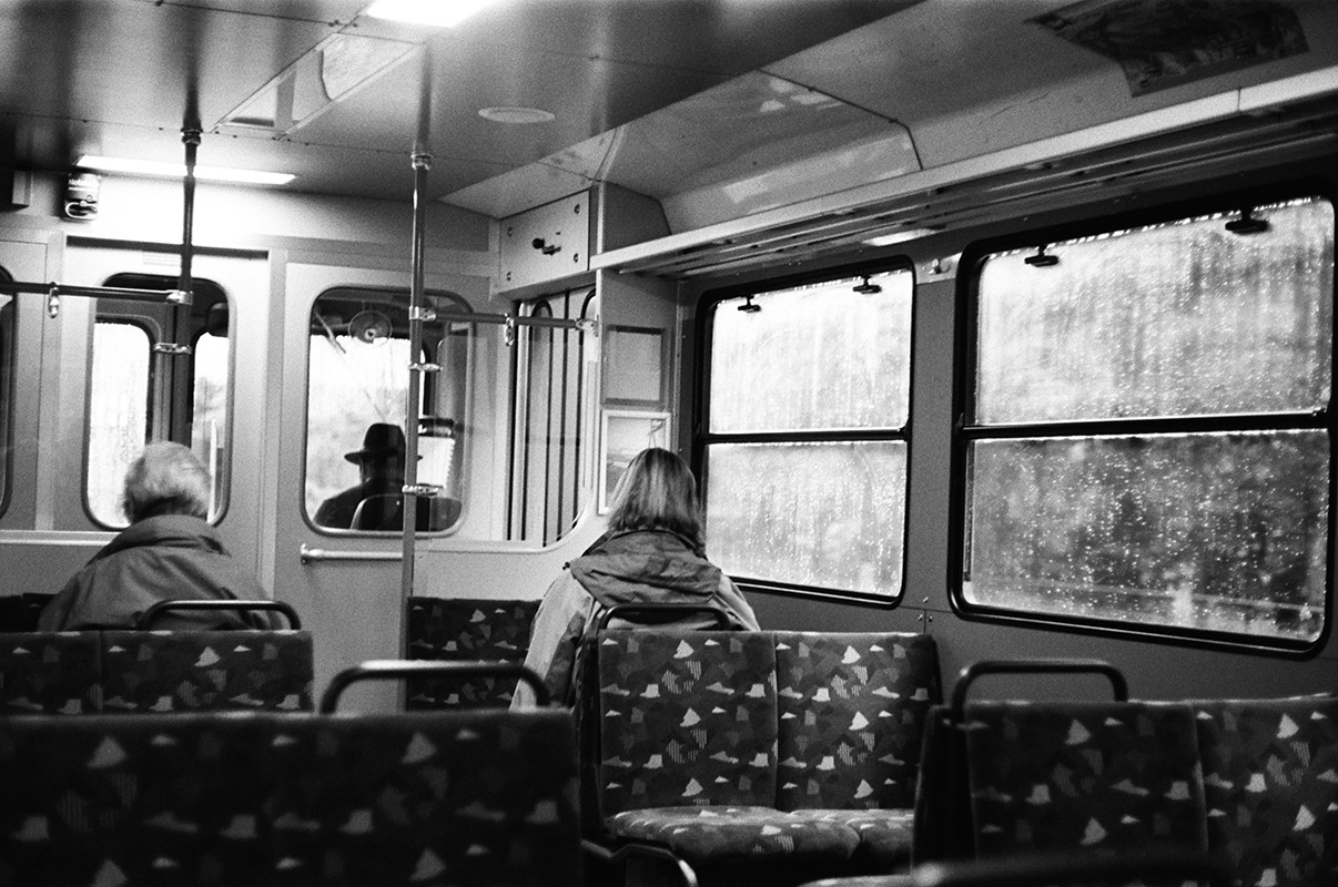 the interior of a cogwheel train car. it's raining outside. the driver is wearing a hat while two other passengers are visible at the front of the car.